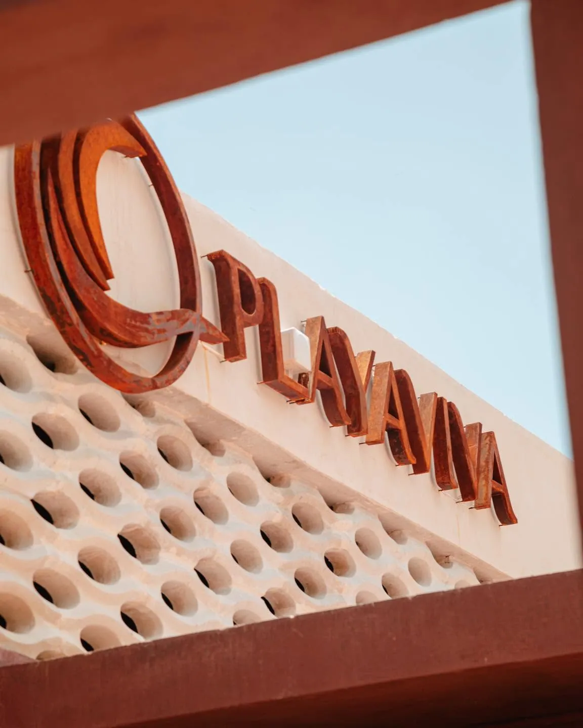 Letrero de Playaviva Beach Club en acero sobre la celosía, contra el cielo